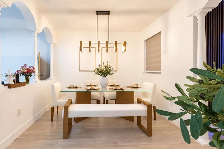 Dining area featuring structural architectural columns, decorative interior archways, wood-finish flooring, and a linear pendant light fixture