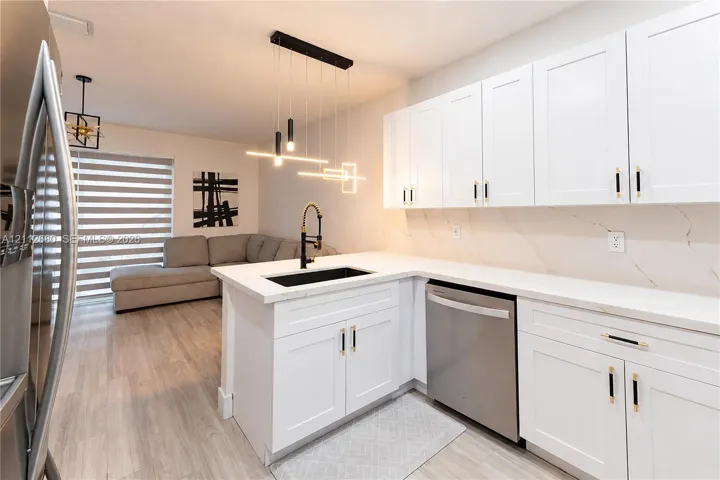 Kitchen featuring white shaker-style cabinetry, quartz countertops with integrated backsplash, matte black hardware, stainless steel dishwasher, and modern linear pendant lighting