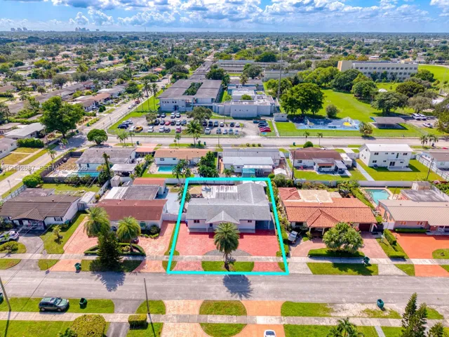 Aerial perspective of a single-story residence featuring a shingled roof, a paved front driveway, a prominent palm tree, and a fenced backyard