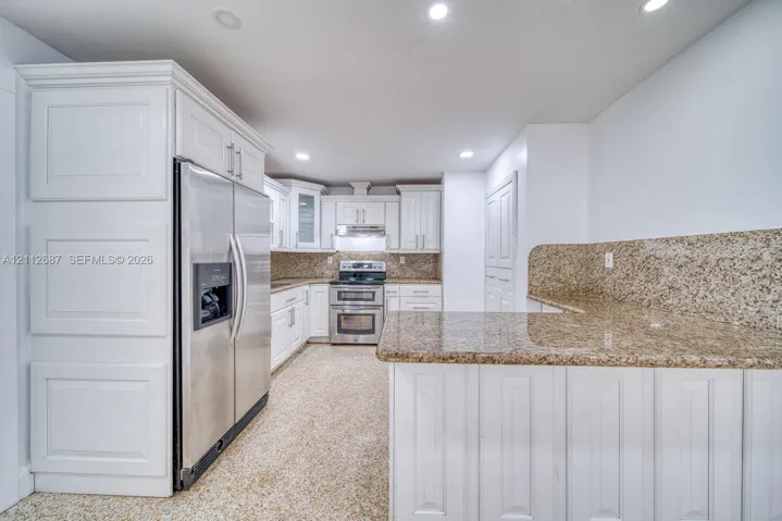 Kitchen featuring custom white cabinetry, stone countertops with matching backsplash, stainless steel appliances, and recessed lighting