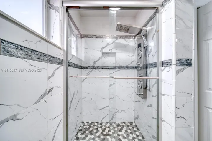 Walk-in shower with floor-to-ceiling veined tile, integrated recessed shelving, multi-head rainfall shower panel, and hexagonal mosaic tile flooring