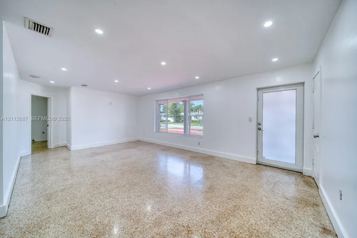 Spacious room featuring polished terrazzo flooring, recessed lighting, and a glass-paneled exterior door