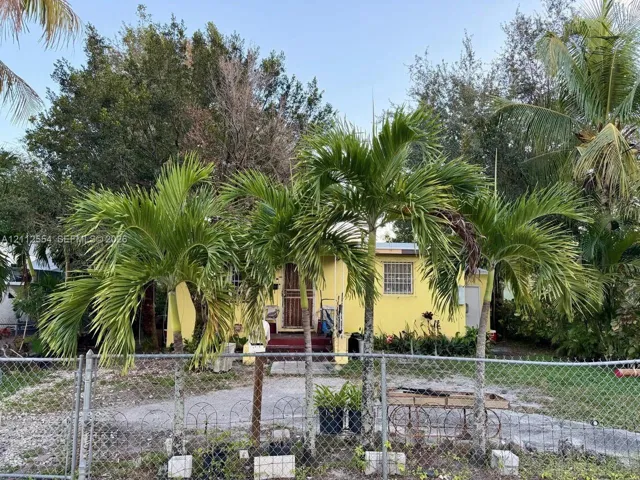 Single-story exterior featuring a stucco facade, mature palm trees, and a chain-link perimeter fence