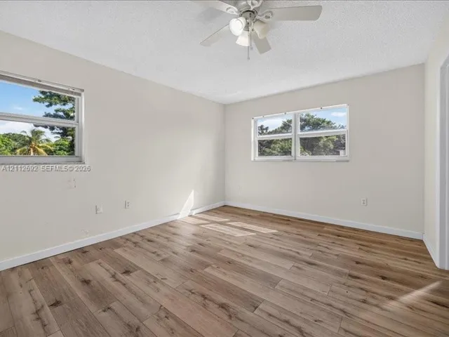 Neutral-toned interior space featuring wood-finish flooring, dual windows, and a ceiling-mounted light fixture with fan