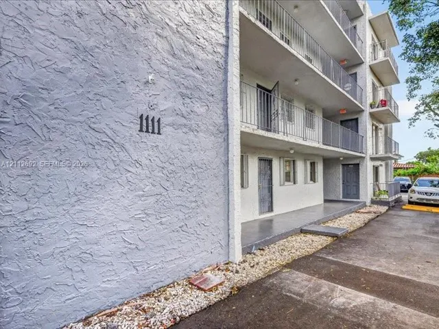Multi-level building exterior featuring textured stucco siding, stacked balconies with metal railings, and a gravel border