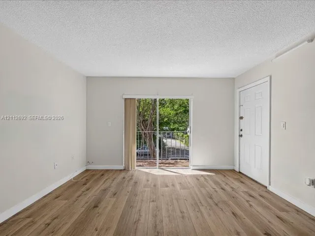 Living area featuring wood-finish flooring, neutral wall paint, and sliding glass doors with access to an exterior balcony
