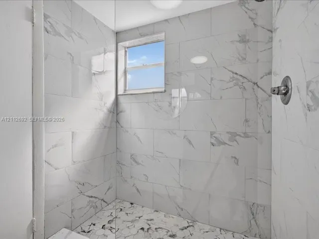 Walk-in shower featuring large-format porcelain wall tile, hexagonal floor tile, a recessed window, and a wall-mounted faucet fixture