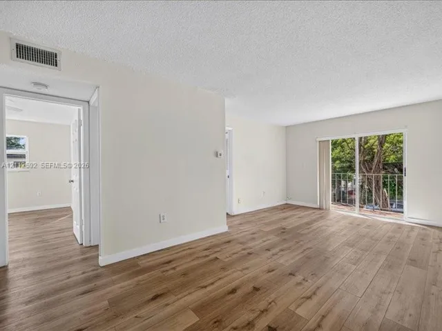 Open-concept interior featuring wood-finish flooring, neutral wall paint, and sliding glass doors with exterior railing