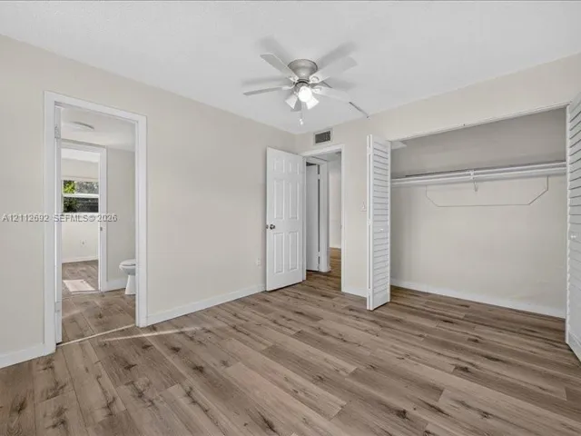 Room featuring wood-finish flooring, a ceiling fan with integrated lighting, and a closet with bifold louvered doors