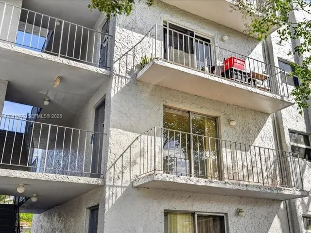Multi-story exterior featuring a textured stucco facade, stacked private balconies with metal railings, and sliding glass door entries