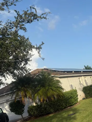 Exterior featuring a tiled roof with integrated solar panels, stucco siding, and mature landscaping