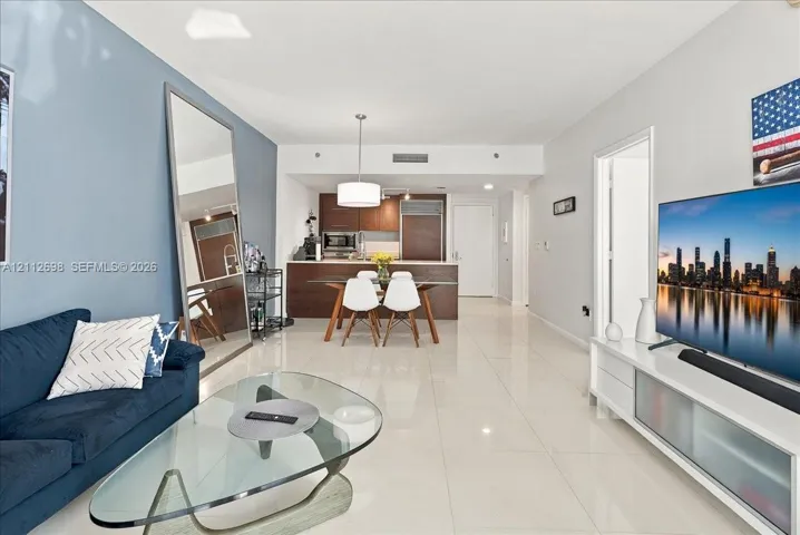 Open-concept interior featuring light-toned tile flooring, recessed lighting, and kitchen cabinetry with a dark wood-finish