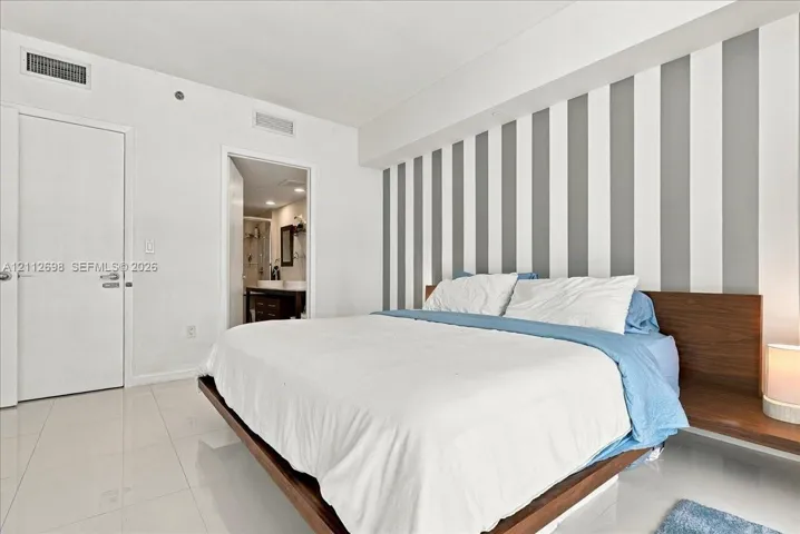 Polished tile flooring, vertical wall accent detailing, and built-in wood-finish headboard with integrated side tables