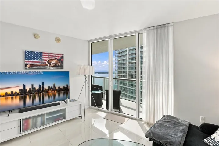 Floor-to-ceiling glass sliding doors, polished tile flooring, and a covered balcony overlooking the water and metropolitan skyline