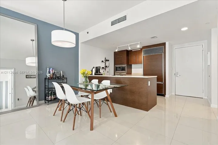 Open-concept interior featuring large-format tile flooring, built-in cabinetry with wood-finish paneling, an integrated refrigerator, recessed track lighting, and an oversized wall mirror