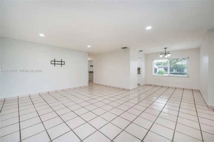 Open-concept room featuring light-toned tile flooring, recessed ceiling lighting, a multi-arm chandelier, and a large window