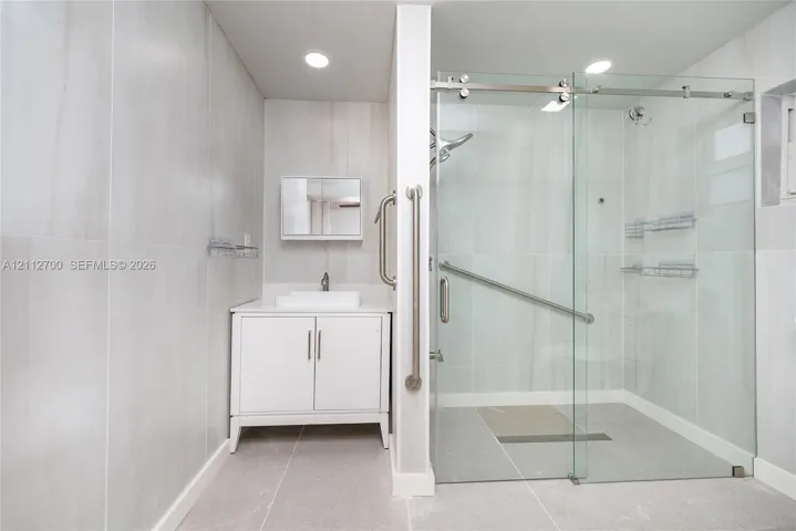 Bathroom featuring large-format wall tile, white vanity cabinet with a rectangular vessel sink, walk-in shower with glass sliding doors, and brushed nickel hardware