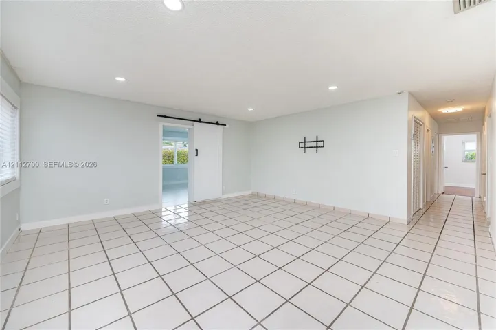 Open-concept interior featuring large-format tile flooring, recessed lighting, and a white sliding barn door with black hardware