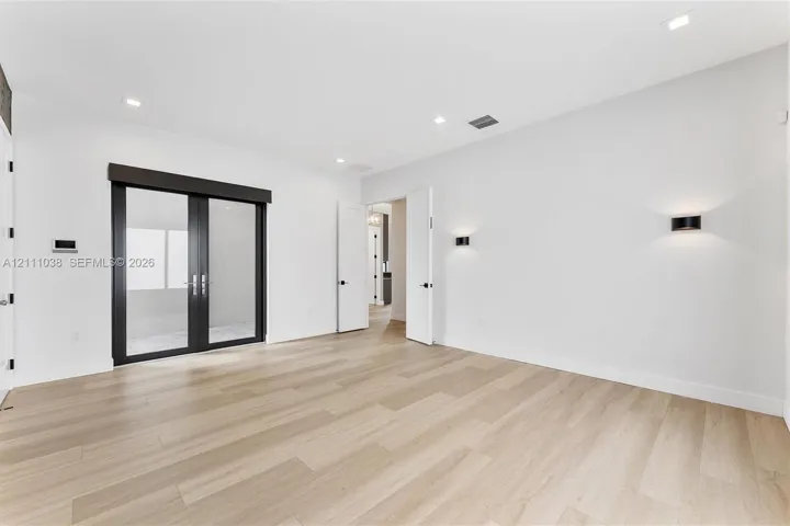 Room featuring light wood-finish flooring, recessed lighting, matte black wall-mounted fixtures, and glass-paned double doors with a dark frame