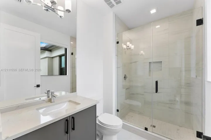Bathroom featuring a vanity with stone-finish countertop, undermount sink, frameless glass-enclosed shower with floor-to-ceiling tile, and matte black hardware