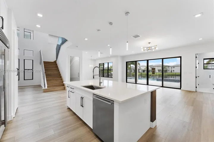 Open-concept kitchen featuring a center island with a quartz countertop, stainless steel dishwasher, and under-mount sink, complemented by wood-finish flooring, recessed lighting, and multi-panel sliding glass doors