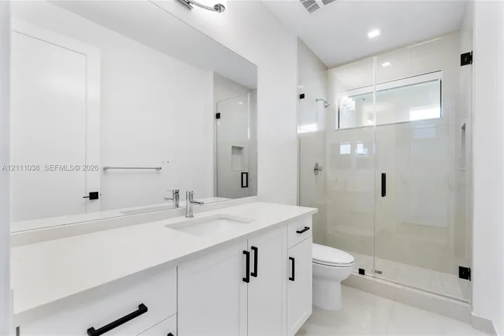 White cabinetry vanity with solid surface countertop, glass-enclosed shower with tiled walls and built-in niche, and matte black hardware fixtures