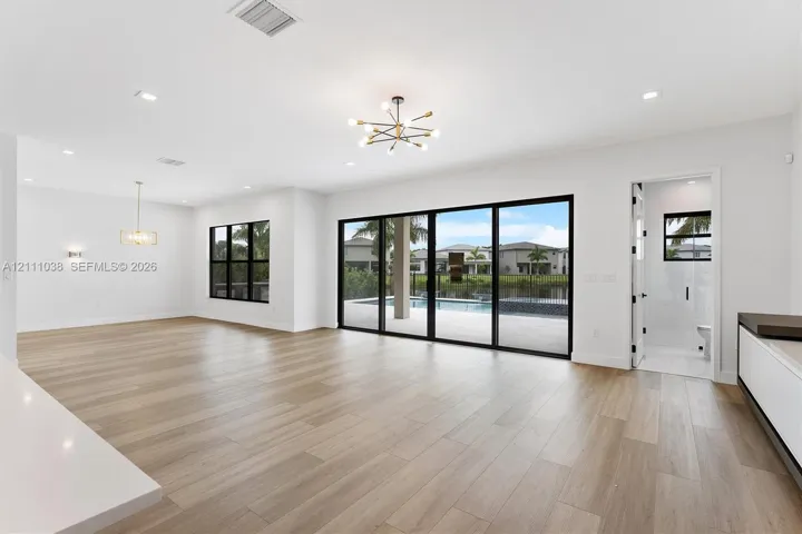 Open-concept interior featuring light wood-finish flooring, multi-panel sliding glass doors with black frames, recessed lighting, and modern multi-arm chandeliers