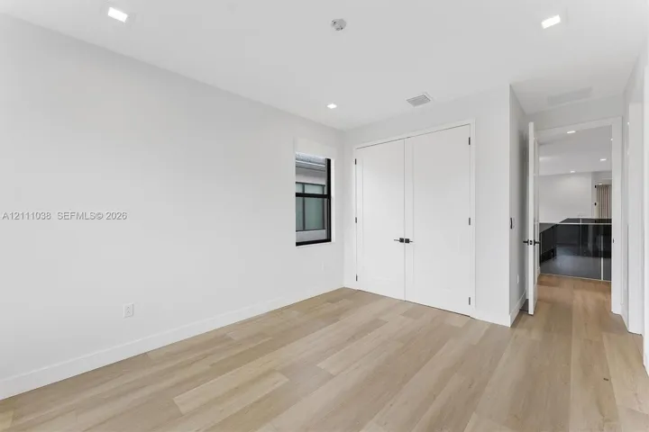 Neutral-toned interior featuring wood-finish flooring, recessed lighting, white double closet doors with matte black hardware, and a window with a black frame