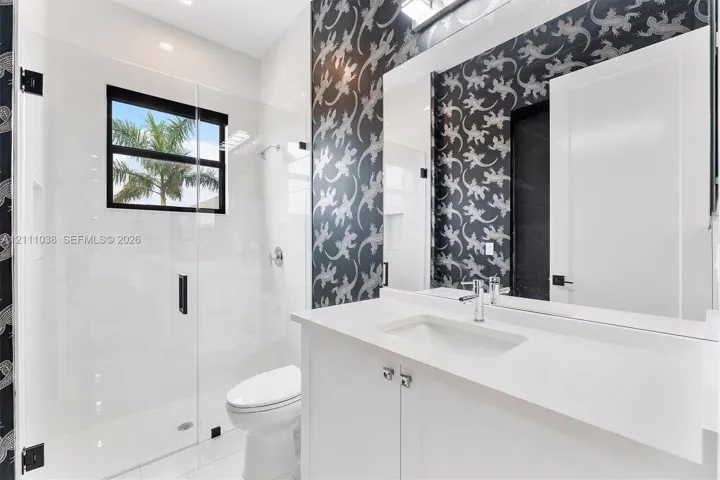 Bathroom featuring a white vanity with a quartz countertop, frameless glass-enclosed shower, polished chrome fixtures, and patterned wallcovering