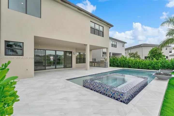 Rear exterior featuring a covered patio, swimming pool with integrated spillover spa, tiled water feature, and built-in outdoor kitchen