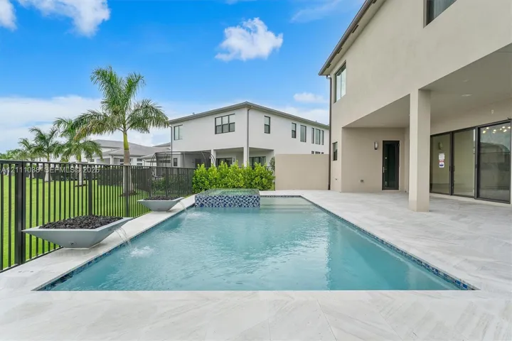 Swimming pool with a raised spa, decorative stone spillover bowls, neutral-toned tiled decking, and a black metal perimeter fence