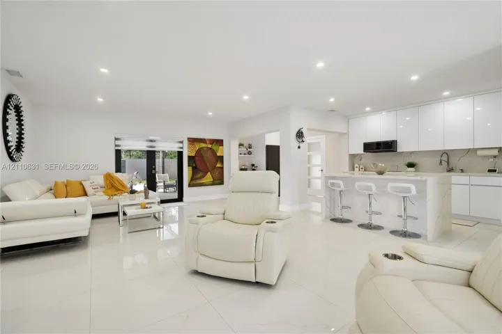 Open-concept kitchen featuring high-gloss cabinetry, stone-finish countertops, waterfall-edge island, large-format tile flooring, and recessed lighting
