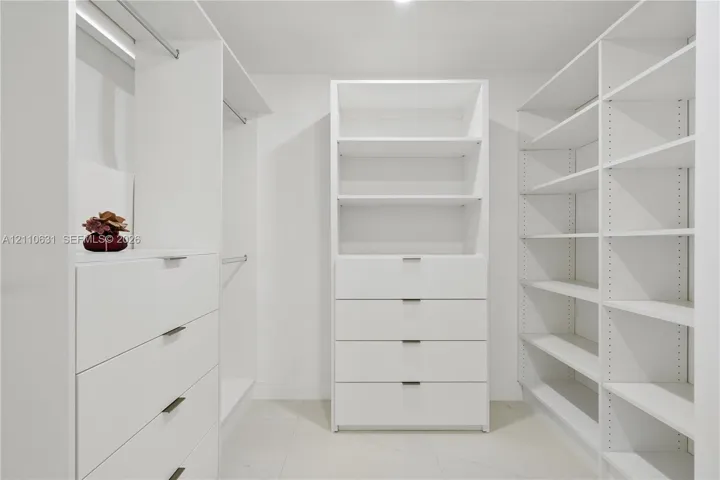 Custom walk-in closet featuring white built-in cabinetry, integrated shelving units, deep-drawers with modern pulls, and hanging rods