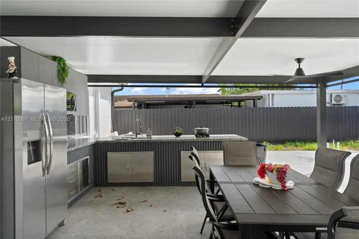 Covered outdoor kitchen featuring a stone-topped island, stainless steel cabinetry, built-in refrigerator, recessed lighting, and a ceiling fan