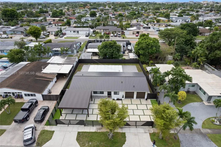 Aerial perspective featuring a metal roof, attached carport, multi-car garage, perimeter fencing, and paver driveway