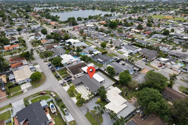 Aerial perspective of a property featuring a dark-toned gable roof, a concrete paver driveway with grass inlay, a metal-framed carport, and mature perimeter trees