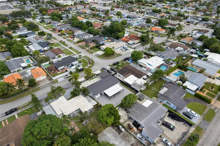 Aerial perspective of a property featuring a dark-toned metal roof, a paved driveway, and a covered carport