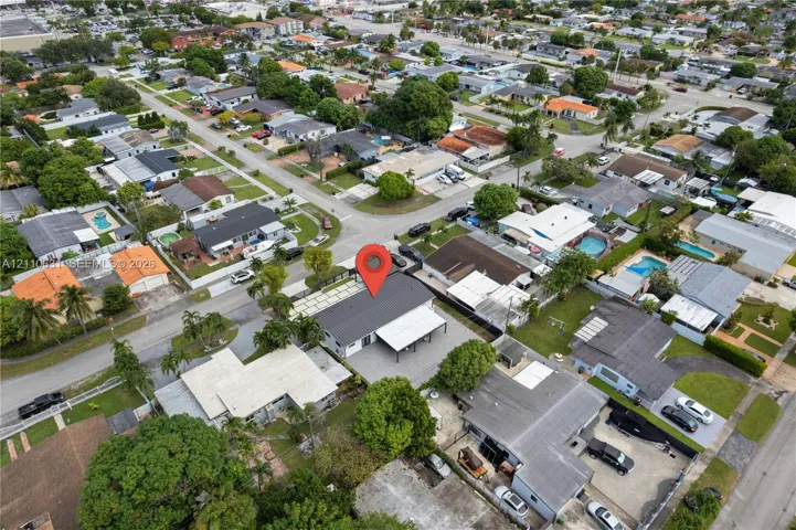 Aerial perspective of residential property featuring a metal roof, an attached covered carport, a paved driveway, and perimeter fencing