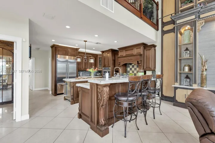 Kitchen featuring stained wood cabinetry, stone countertops, a multi-level breakfast bar with carved corbels, recessed lighting, and stainless steel appliances