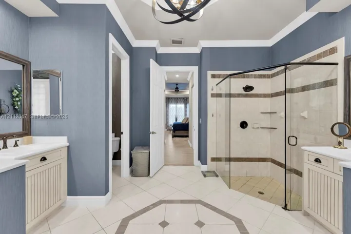 Dual vanities with white cabinetry, corner glass-enclosed shower featuring tile surround and stone-tile flooring, and modern metal hardware finishes