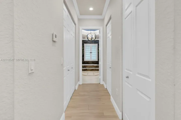 Hallway featuring wood-finish flooring, recessed ceiling lighting, crown molding, and double-door closets with chrome hardware