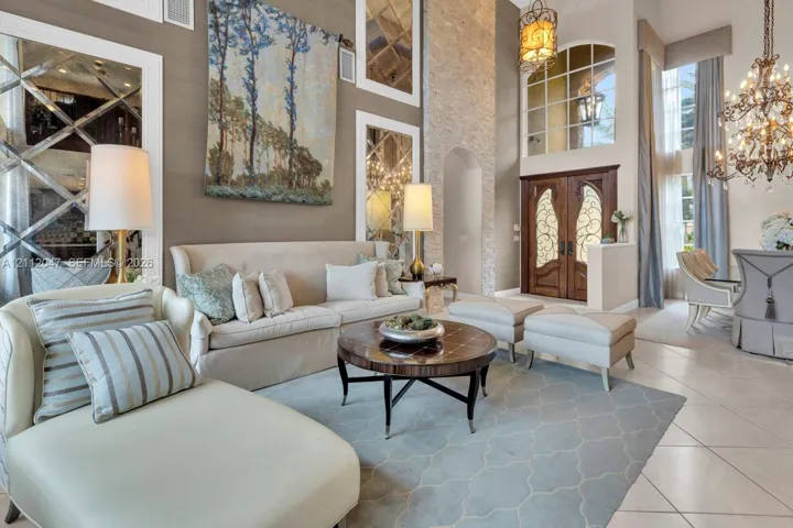 Two-story living area featuring a floor-to-ceiling stone fireplace, decorative mirrored wall panels, dual wrought-iron and wood entry doors, and an ornate multi-tiered crystal chandelier