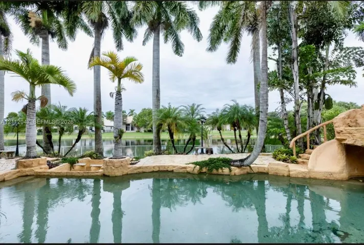 Waterfront pool area featuring natural stone coping, a built-in stone slide, paver decking, and mature palm trees