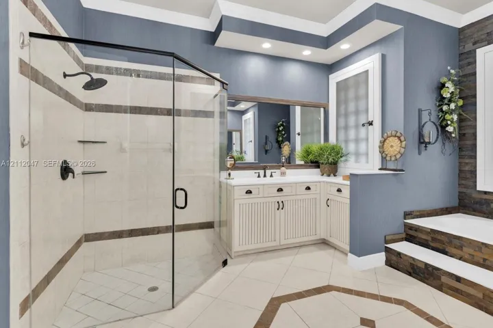 Bathroom featuring a corner glass-enclosed shower, stone tile accents, white beadboard cabinetry with a solid-surface countertop, and a built-in soaking tub with stone tile surround