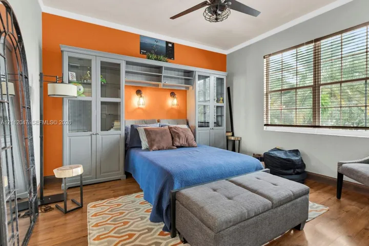 Custom built-in grey cabinetry with glass-front display doors, wood-finish flooring, dual wall-mounted light fixtures, and ceiling fan with integrated lighting