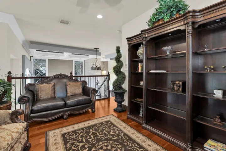Built-in dark wood shelving unit with integrated lighting, wood-finish flooring, coffered ceiling detail, and metal stair railing