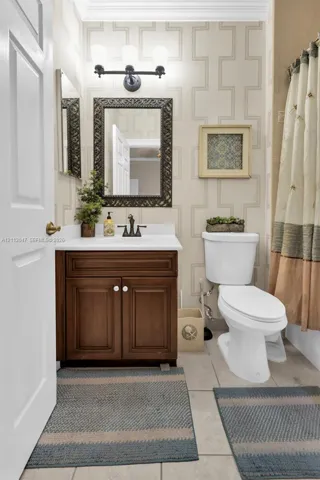 Bathroom featuring a dark wood-finish vanity with a white countertop, three-light vanity fixture, patterned wall covering, and tiled flooring