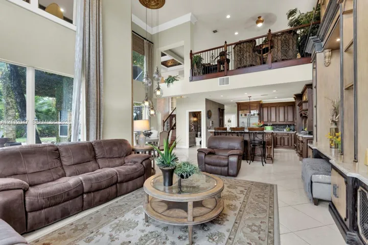 Multi-story living area featuring floor-to-ceiling windows, an elevated gallery overlook with iron railings, coffered ceiling detailing, and built-in cabinetry