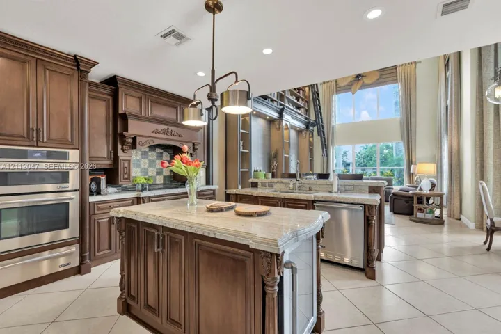 Kitchen featuring stained wood cabinetry, stone countertops, stainless steel double wall ovens, a central island with built-in storage, and tile flooring