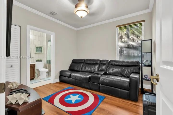 Room featuring wood-finish flooring, crown molding, a central ceiling-mounted light fixture, and a window with horizontal blinds